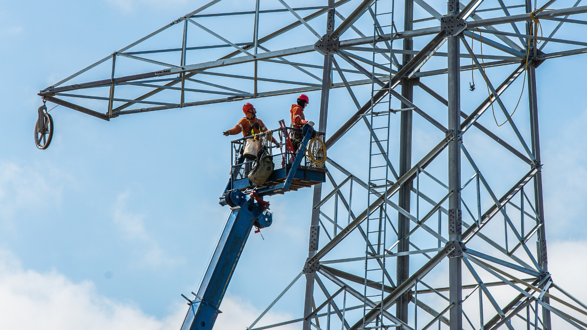 Two construction workers suspended in the air working on a tower